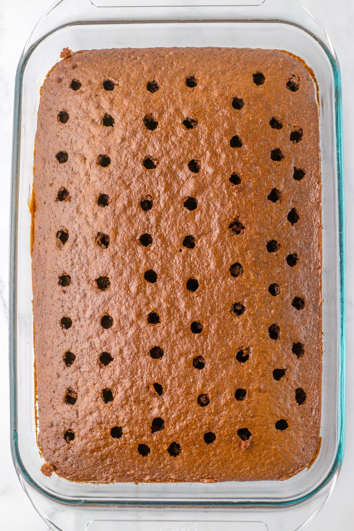 a baked chocolate cake with holes poke evenly out all over it in a glass baking dish