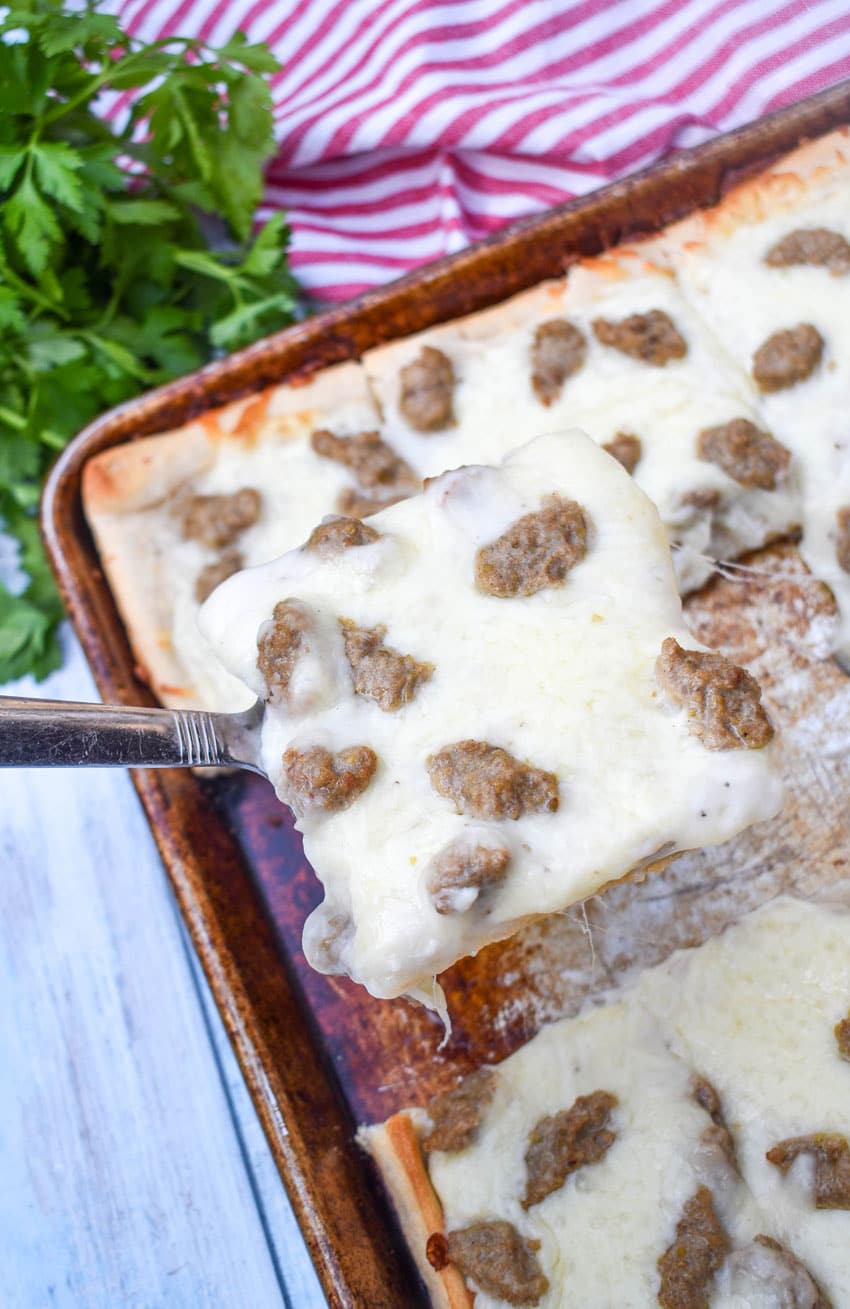 a silver spatula scooping a slice of cafeteria breakfast pizza off a metal baking sheet
