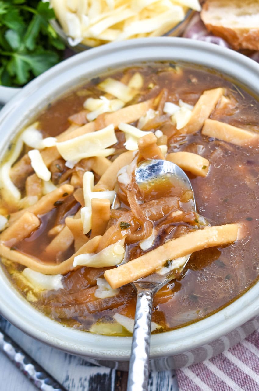 french onion noodle soup topped with shredded swiss cheese in a gray bowl