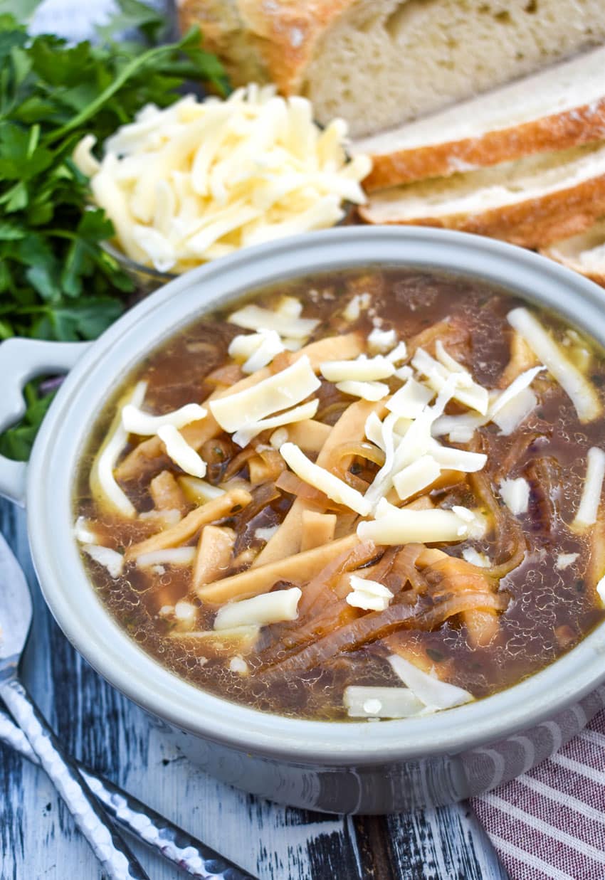 french onion noodle soup topped with shredded swiss cheese in a gray bowl