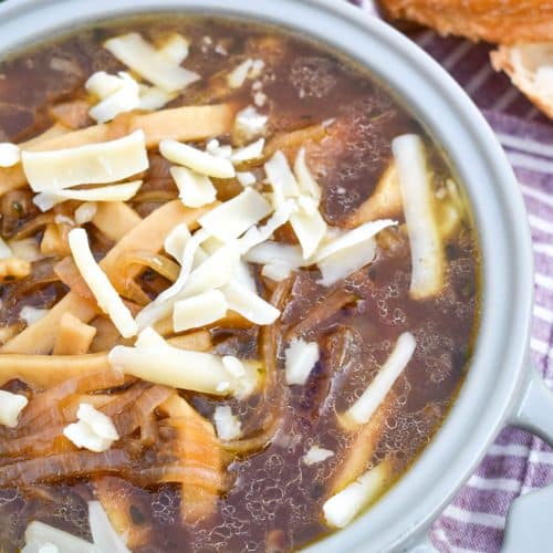 french onion noodle soup topped with shredded swiss cheese in a gray bowl