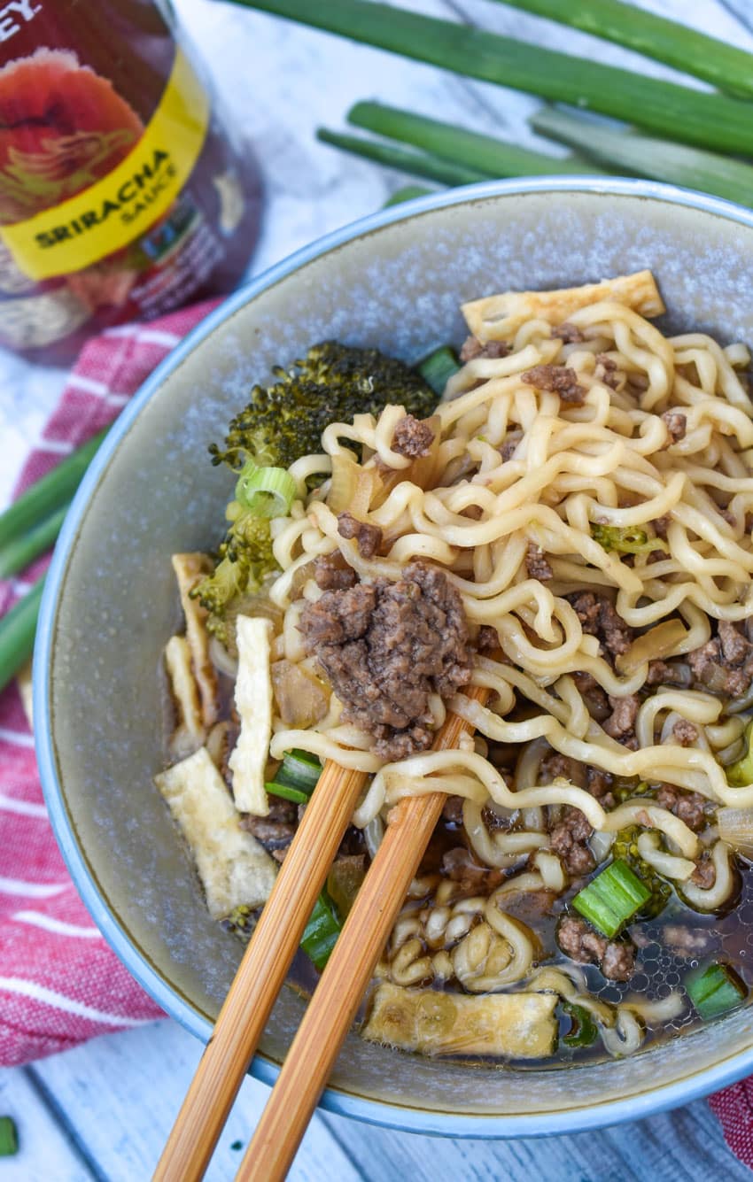 wooden chop sticks scooping ground beef and ramen noodles out of a soup bowl