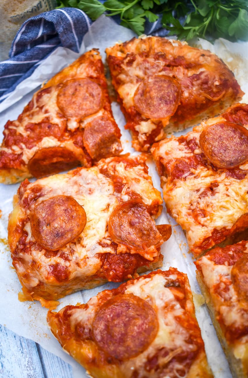 slices of slow cooker pizza on white parchment paper with fresh herbs in the background