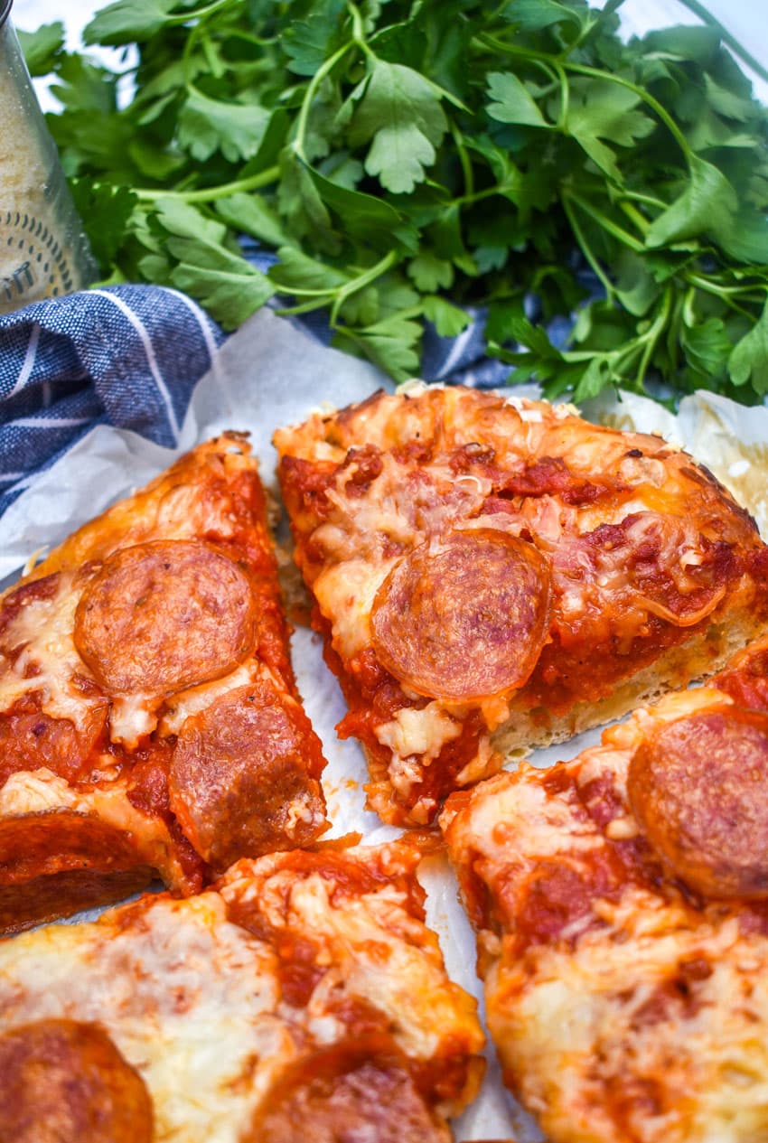 slices of slow cooker pizza on white parchment paper with fresh herbs in the background