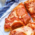 slices of slow cooker pizza on white parchment paper with fresh herbs in the background