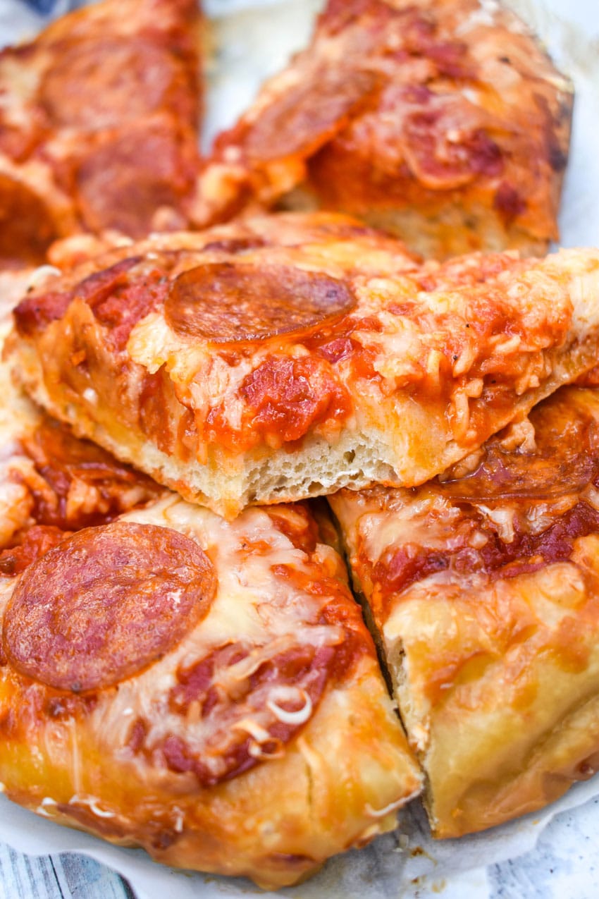 slices of slow cooker pizza on white parchment paper with fresh herbs in the background