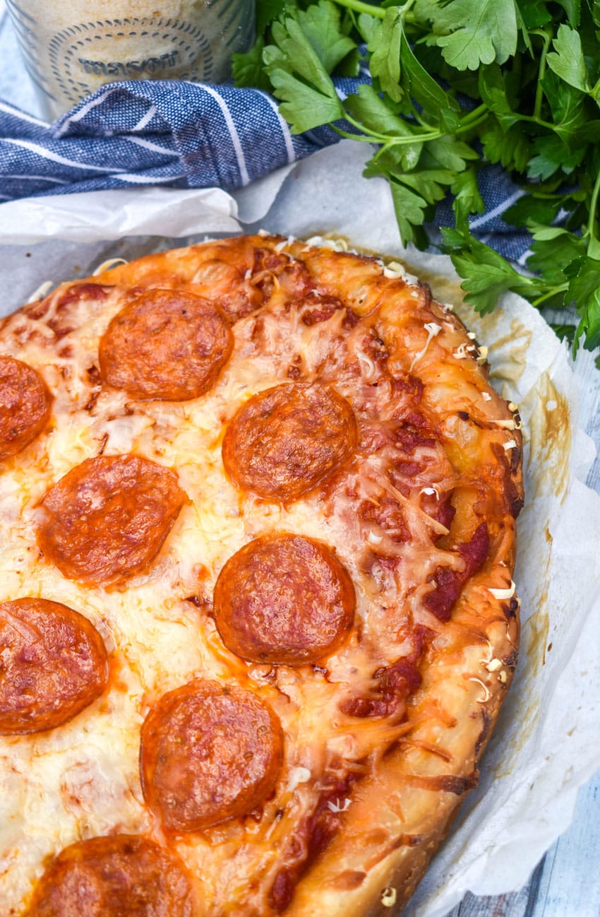 a cooked crockpot pizza on white parchment paper with fresh herbs in the background