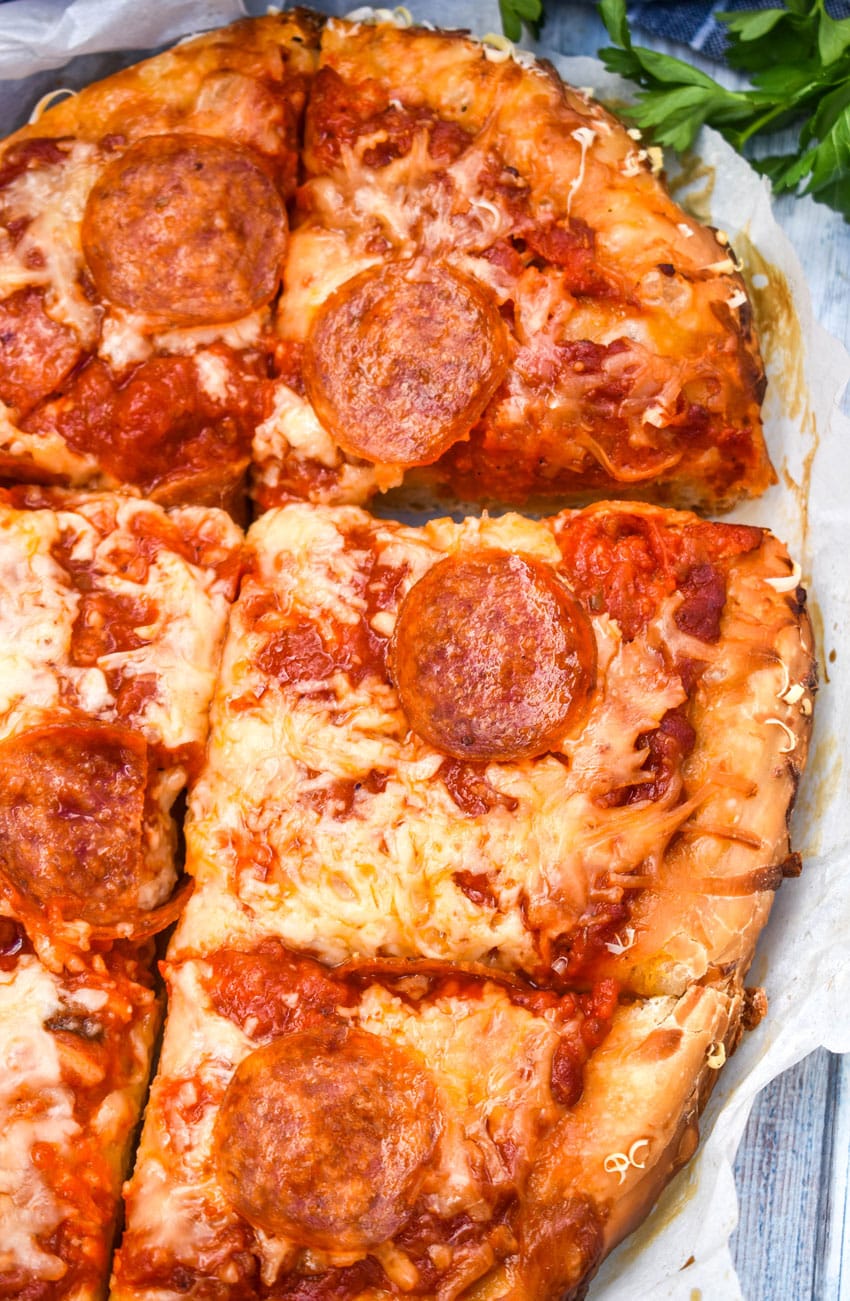 slices of slow cooker pizza on white parchment paper with fresh herbs in the background