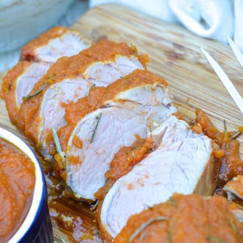 SLICES OF PUMPKIN BUTTER ROASTED PORK TENDERLOIN ON A WOODEN CUTTING BOARD