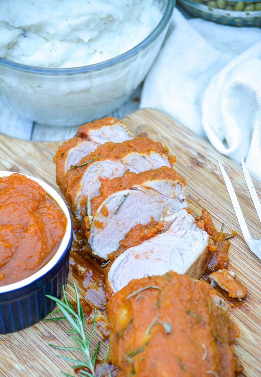 SLICES OF PUMPKIN BUTTER ROASTED PORK TENDERLOIN ON A WOODEN CUTTING BOARD