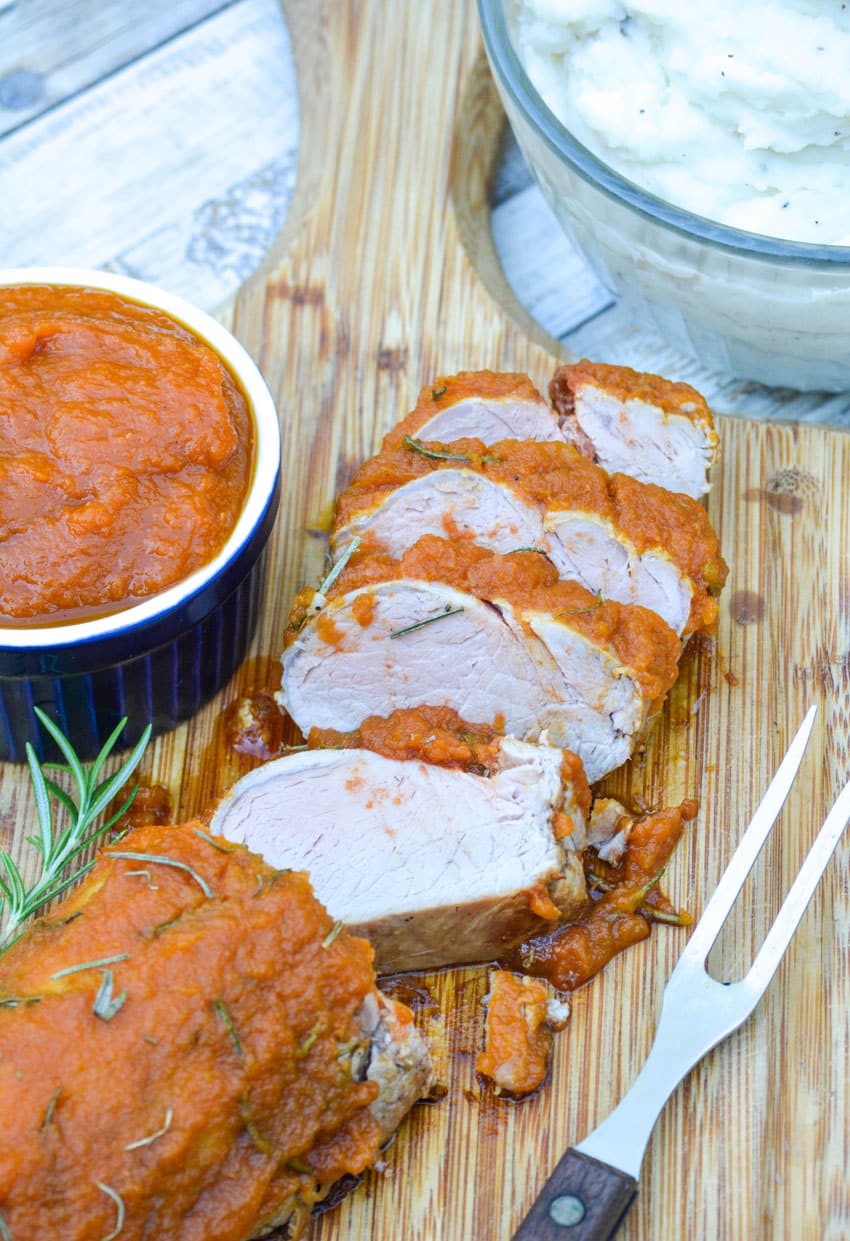 SLICES OF PUMPKIN BUTTER ROASTED PORK TENDERLOIN ON A WOODEN CUTTING BOARD