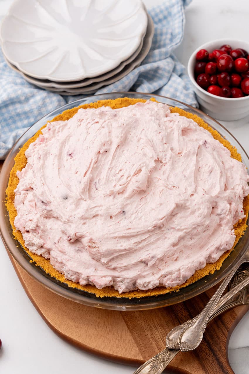 cranberry fluff pie filling in a graham cracker crust on a wooden cutting board