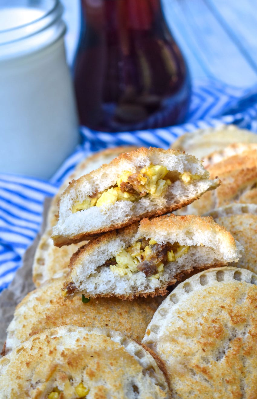 a broken in half breakfast uncrustable revealing the sausage egg and cheese filling is sitting on a pile of uncurstables