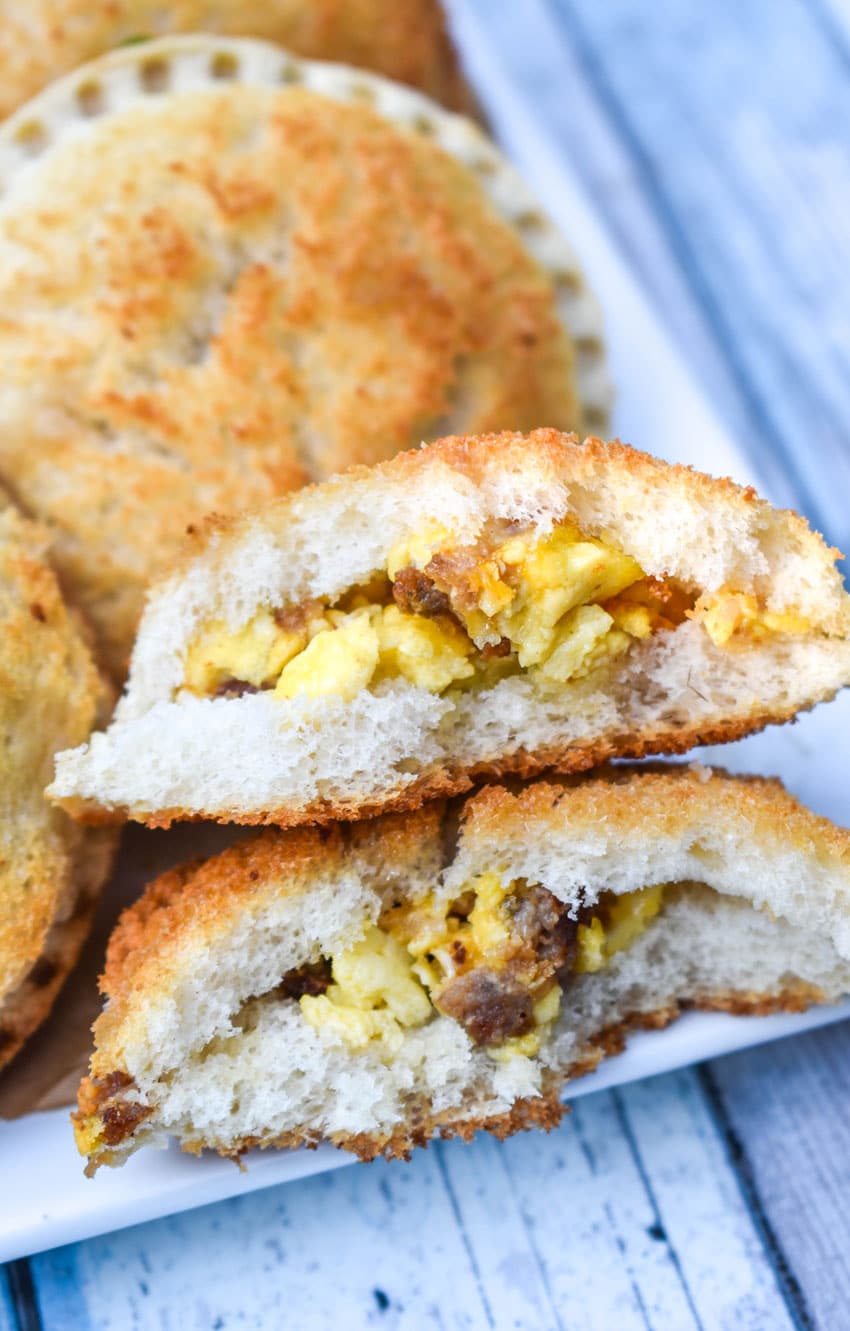 a broken in half breakfast uncrustable revealing the sausage egg and cheese filling resting on the edge of a white serving platter