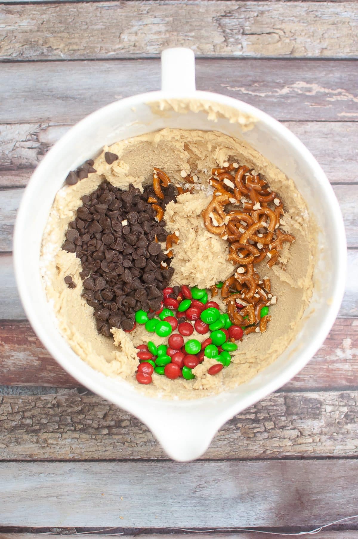 chocolate chips, candy, and broken pretzels sitting in a bowl of cookie dough