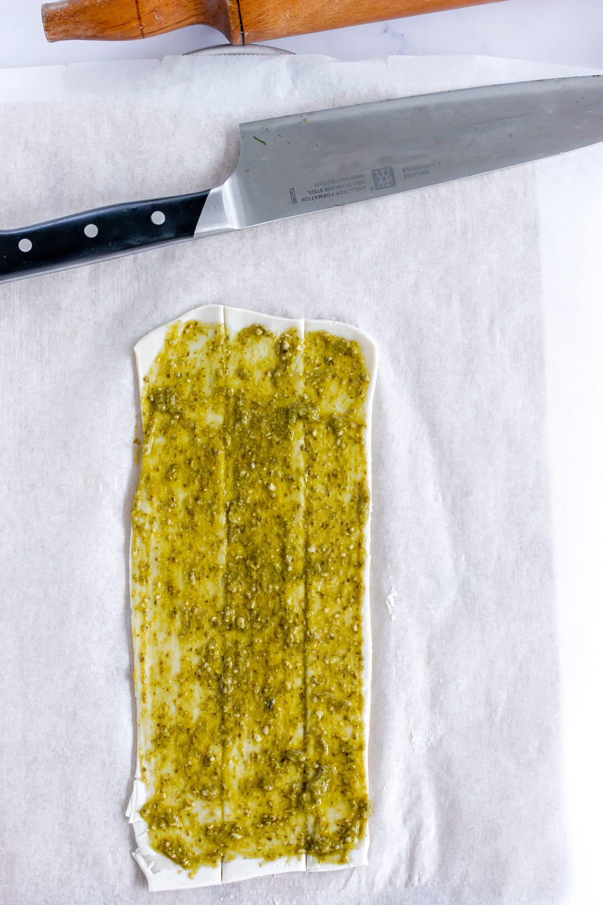 green pesto sauce spread over a sheet of puff pastry