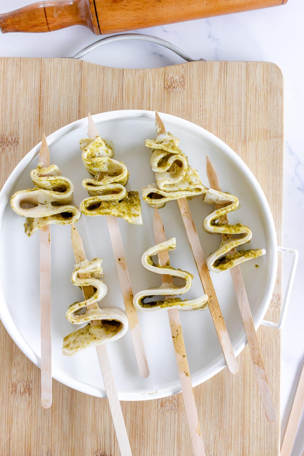 pesto spread ribbons of puff pastry strugn on wooden skewers to resemble trees