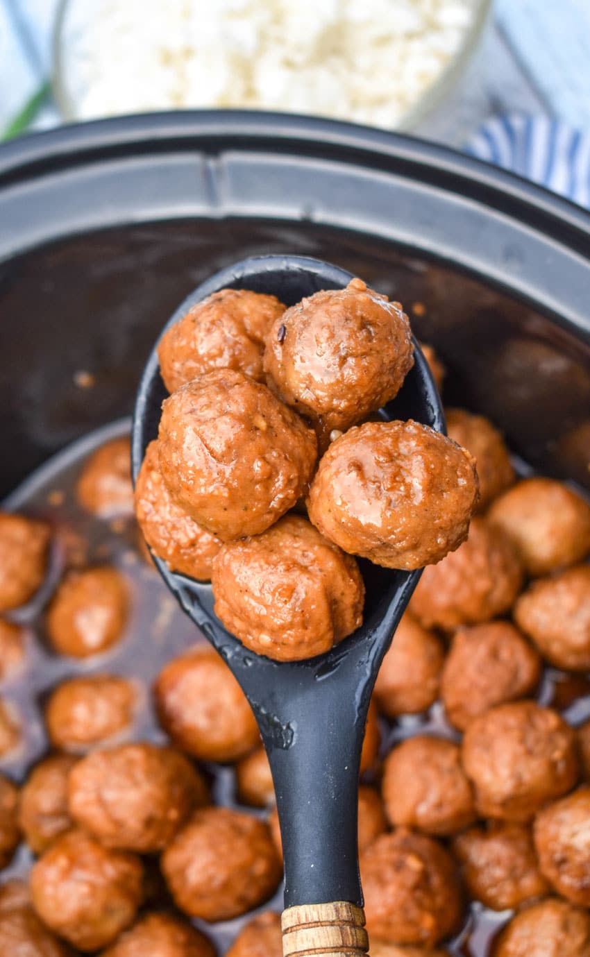 a black wooden handled spoon holding up a scoop of mongolian meatballs