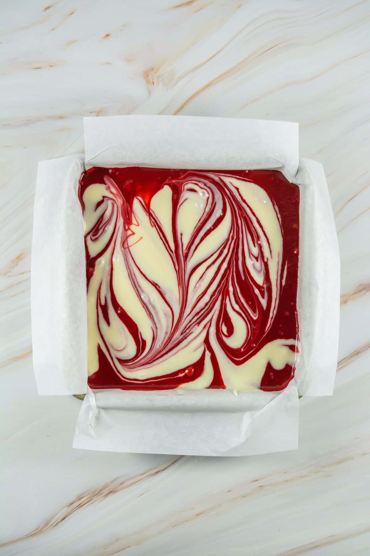 white chocolate swirled with red dyed white chocolate in a parchment paper lined square baking dish