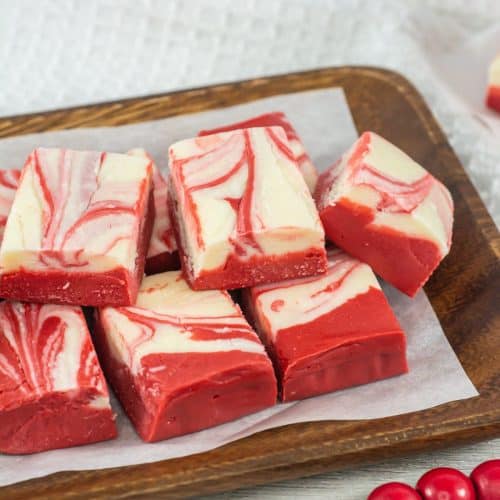 squares of red velvet fudge stacked on a parchment paper lined wooden serving tray