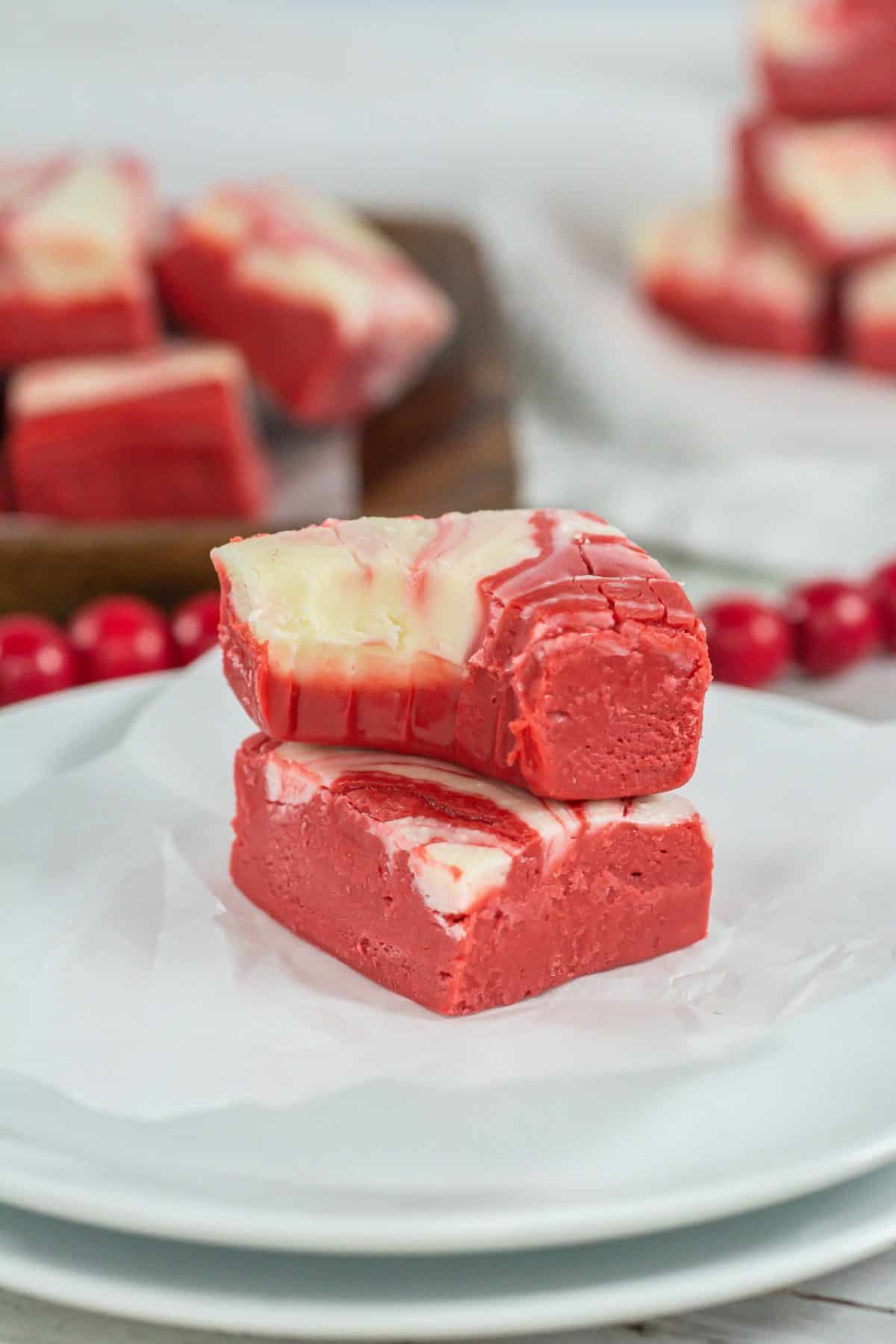 two squares of red velvet fudge stacked on a small square of white parchment paper on a wooden table