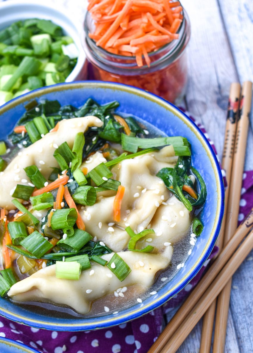 potsticker soup in a blue bowl with wooden chop sticks on the side