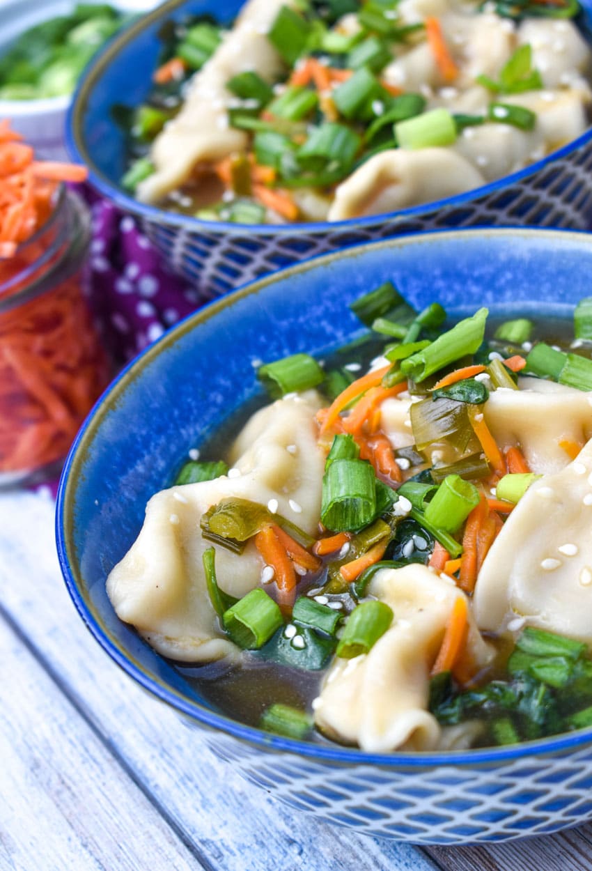 potsticker soup in a blue bowl with wooden chop sticks on the side