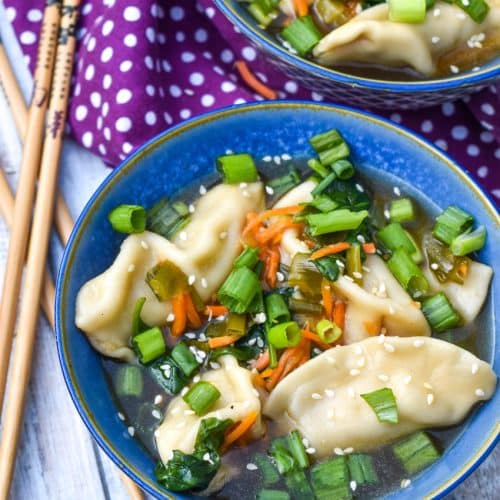 potsticker soup in a blue bowl with wooden chop sticks on the side