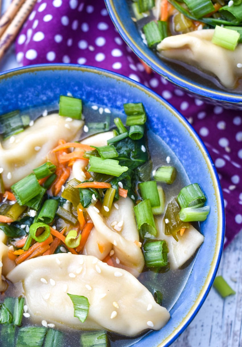 potsticker soup in a blue bowl with wooden chop sticks on the side