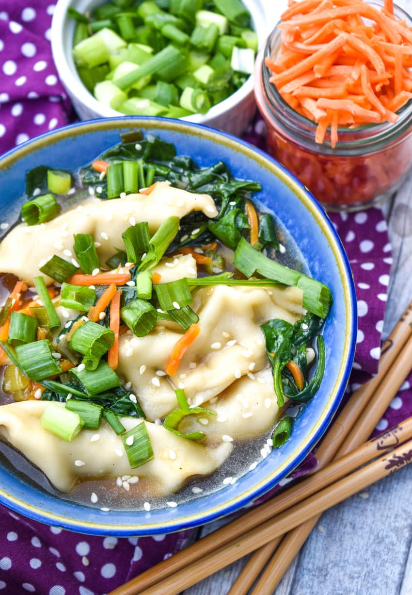 potsticker soup in a blue bowl with wooden chop sticks on the side