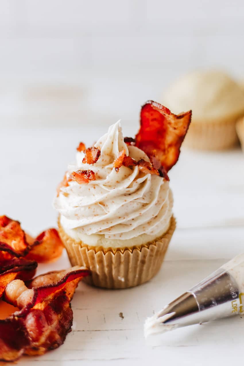 a bacon topped cinnamon frosted pancake muffin on a white tabletop