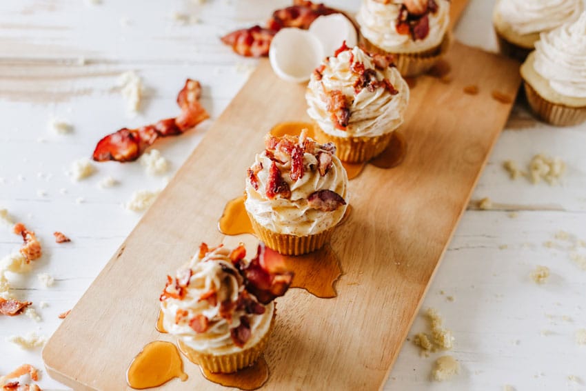 maple bacon pancake muffins drizzled with syrup on a wooden cutting board