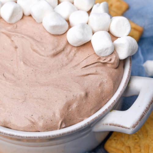 a white bowl filled with hot cocoa dip topped with mini marshmallows
