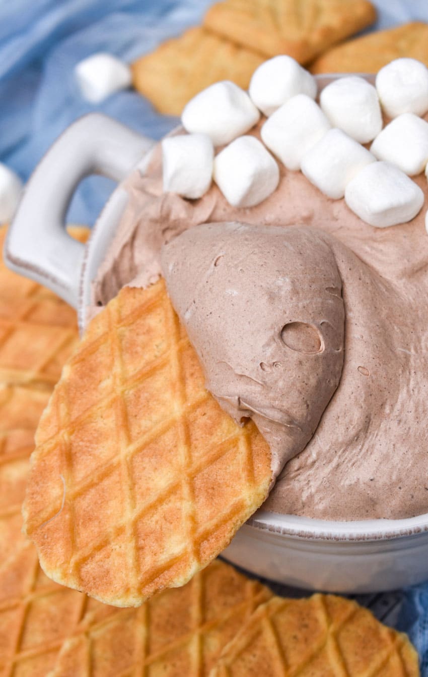 a waffle cookie topped with hot cocoa dip resting on the edge of a white bowl