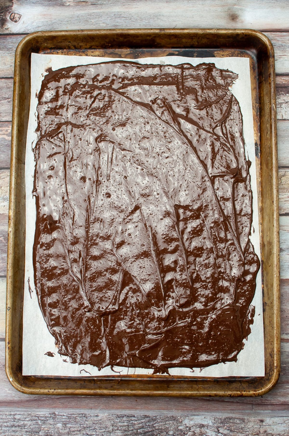 melted mint chocolate spread out over a sheet of parchment paper on a metal baking sheet