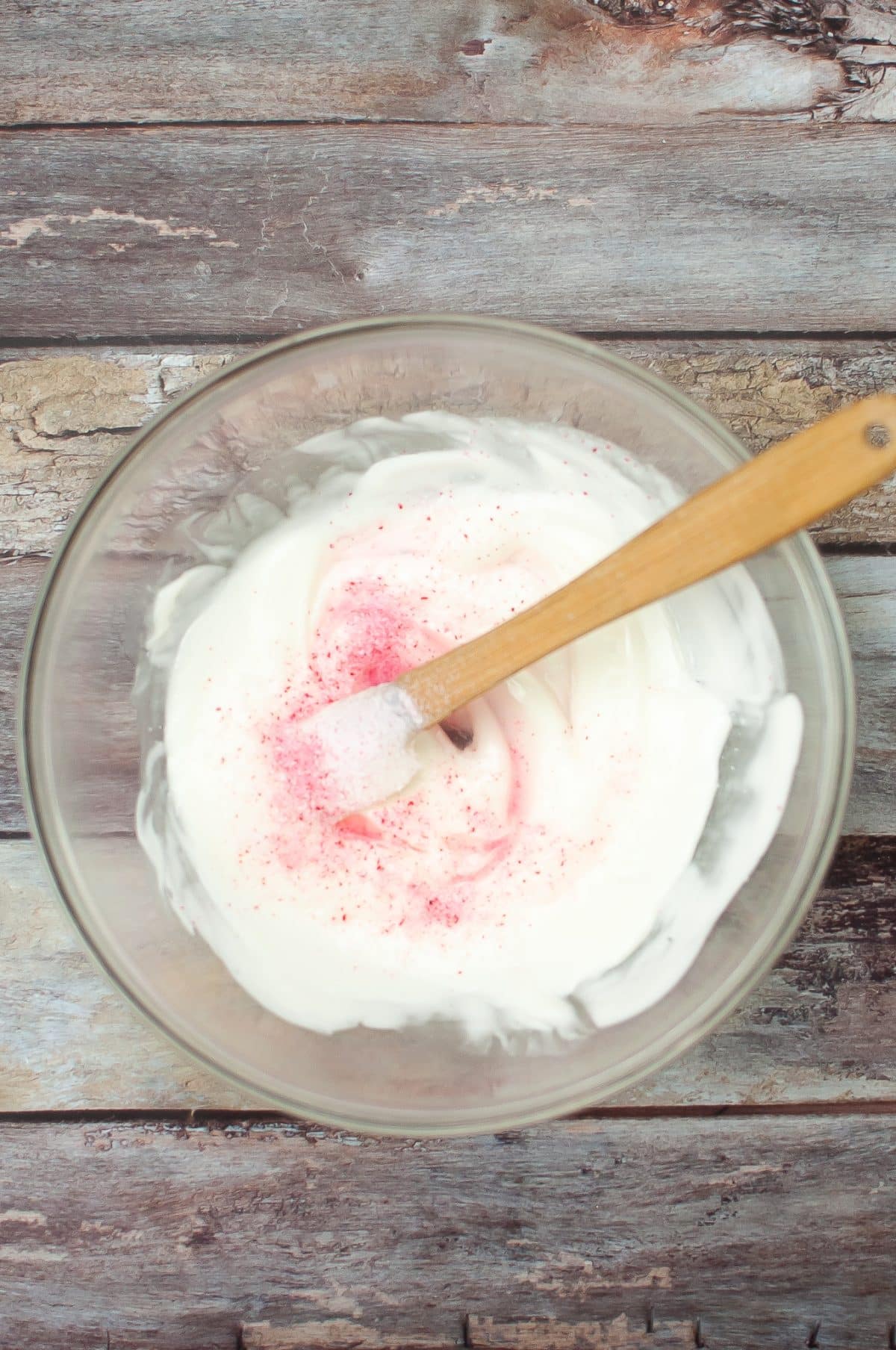 crushed peppermint candy being stirred into melted white chocolate in a glass mixing bowl