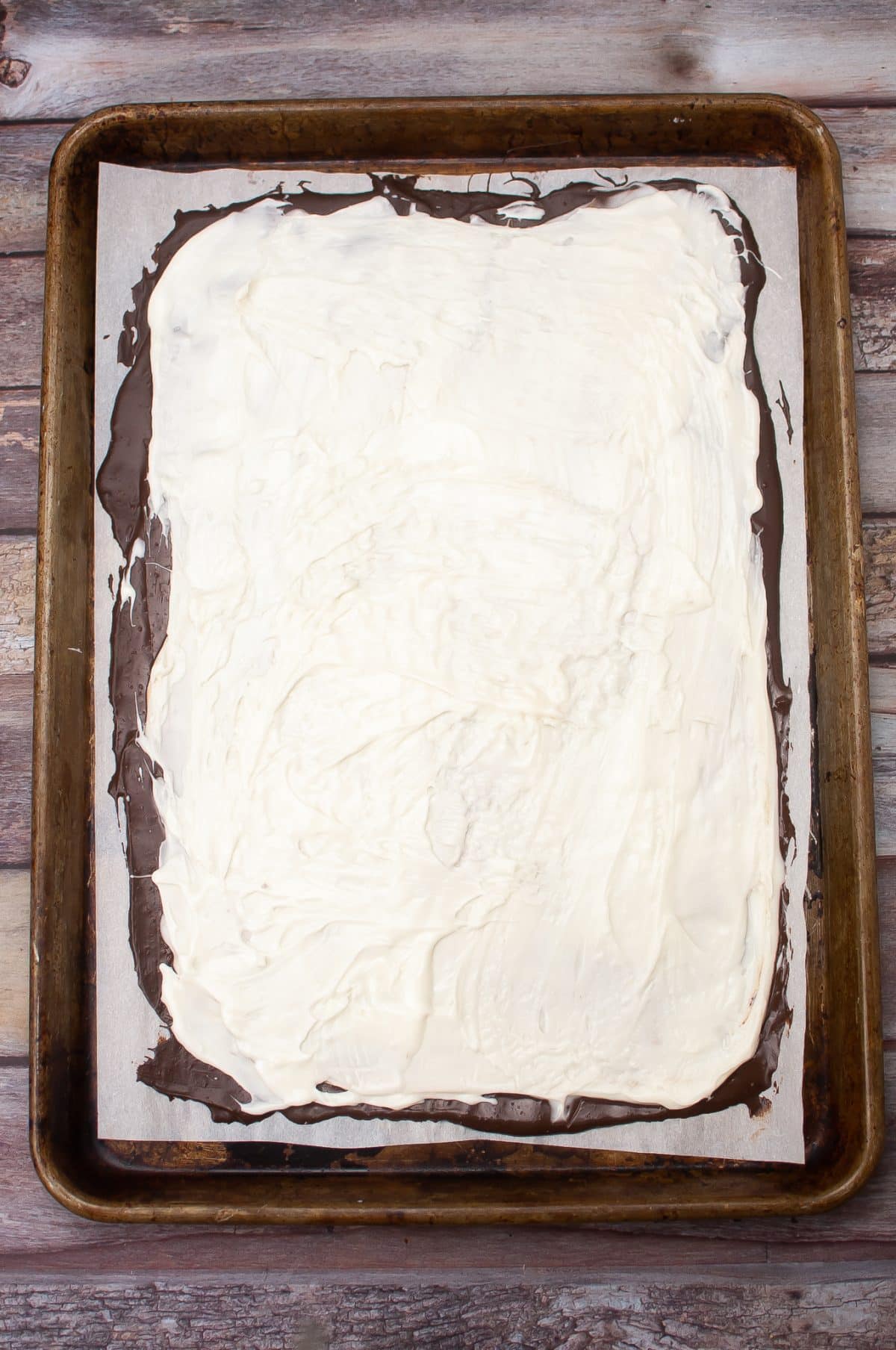 melted white chocolate spread over mint dark chocolate on a parchment lined metal baking sheet