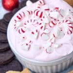 candy cane dip topped with broken pieces of peppermint in a small white ramekin surrounded by cookies