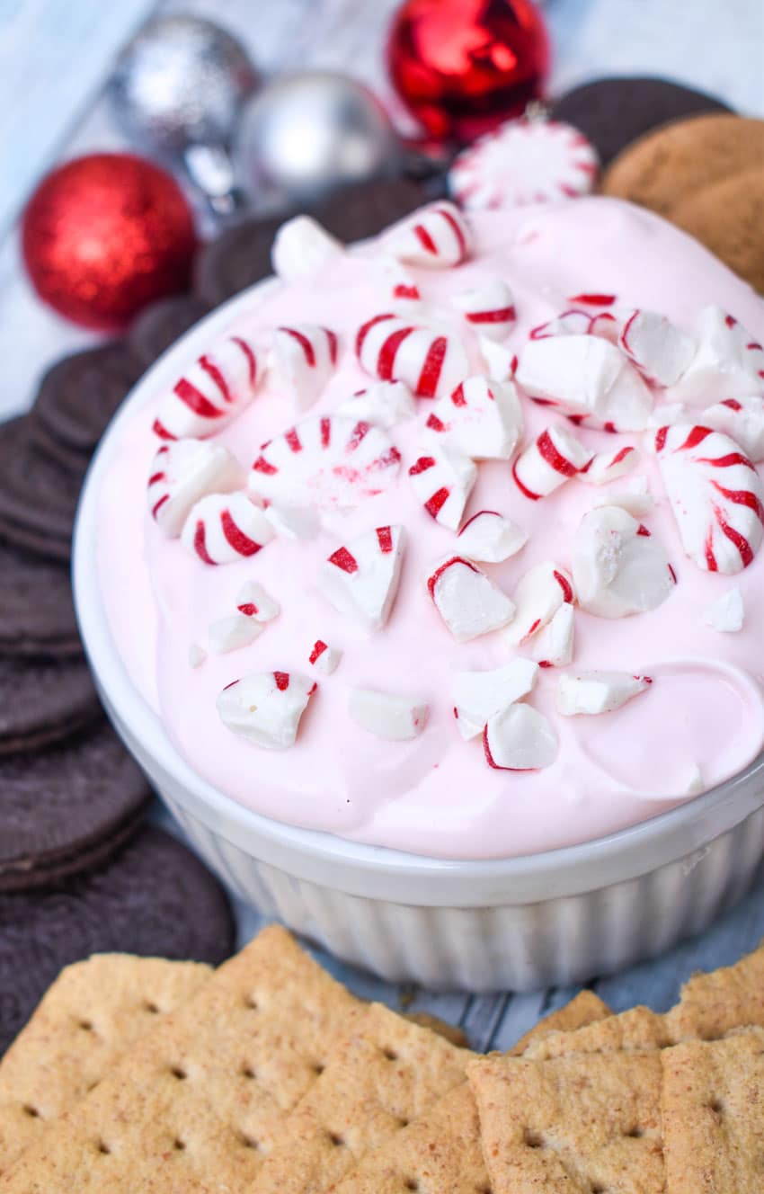 candy cane dip topped with broken pieces of peppermint in a small white ramekin surrounded by cookies