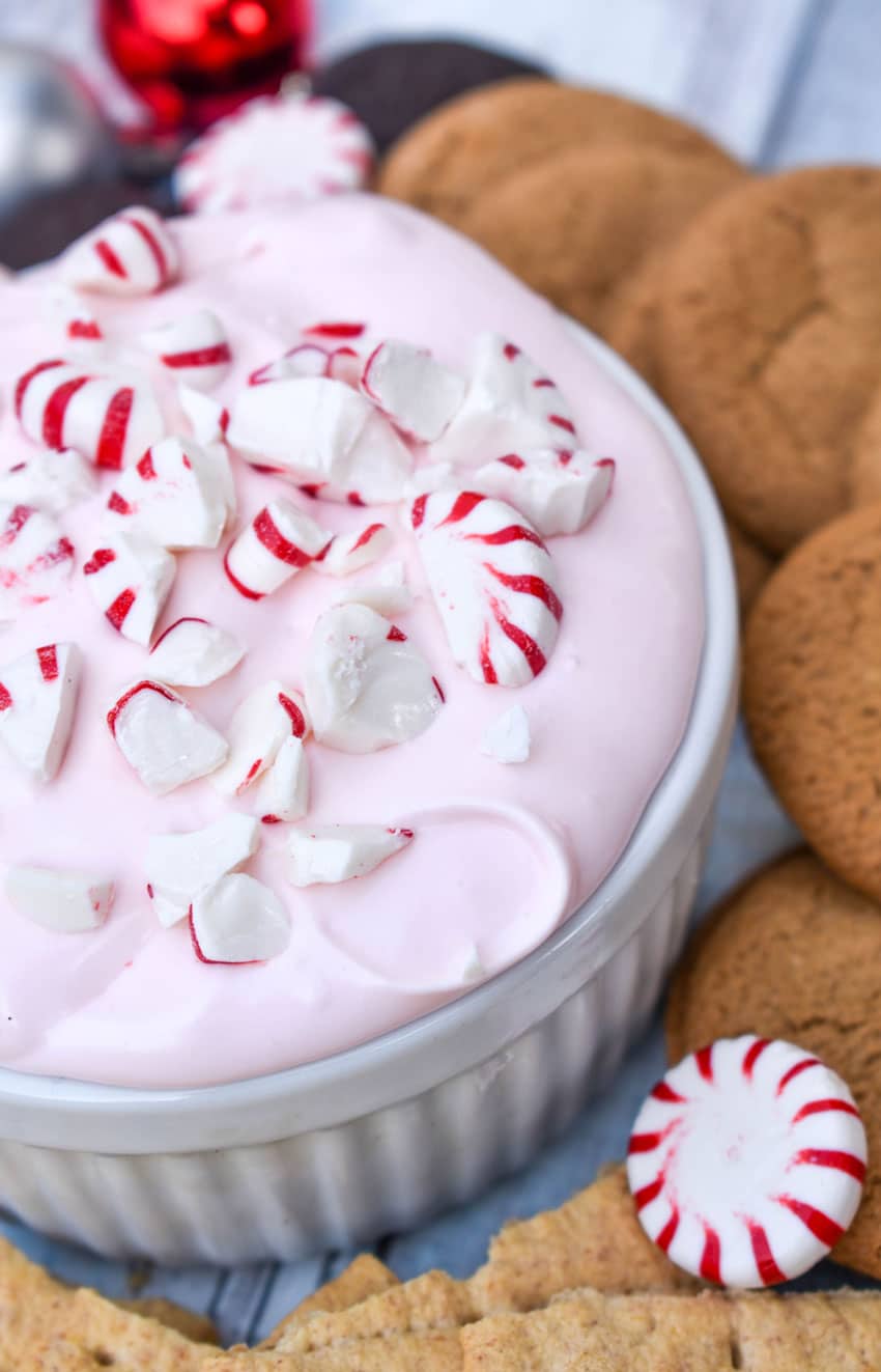 candy cane dip topped with broken pieces of peppermint in a small white ramekin surrounded by cookies