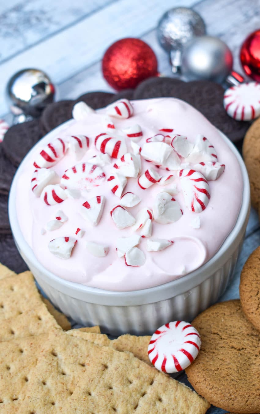 candy cane dip topped with broken pieces of peppermint in a small white ramekin surrounded by cookies