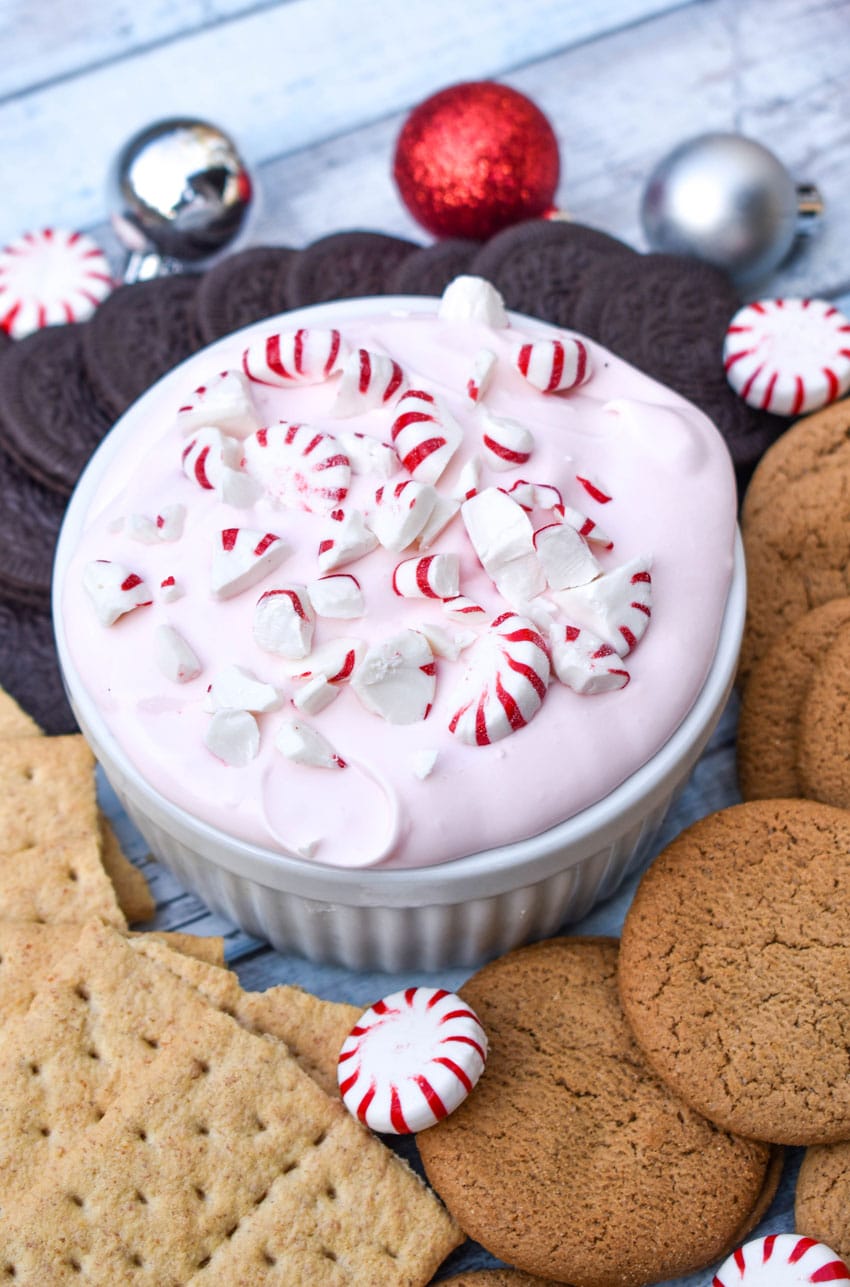 candy cane dip topped with broken pieces of peppermint in a small white ramekin surrounded by cookies