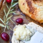 a cheese knife holding a scoop of melted brie cheese resting on a slice of baguette bread