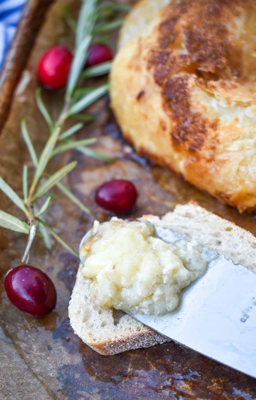 a cheese knife holding a scoop of melted brie cheese resting on a slice of baguette bread
