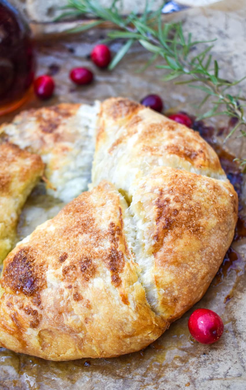 Puff Pastry Wrapped Brie Recipe on a brown parchment paper lined baking sheet with fresh cranberries on the side