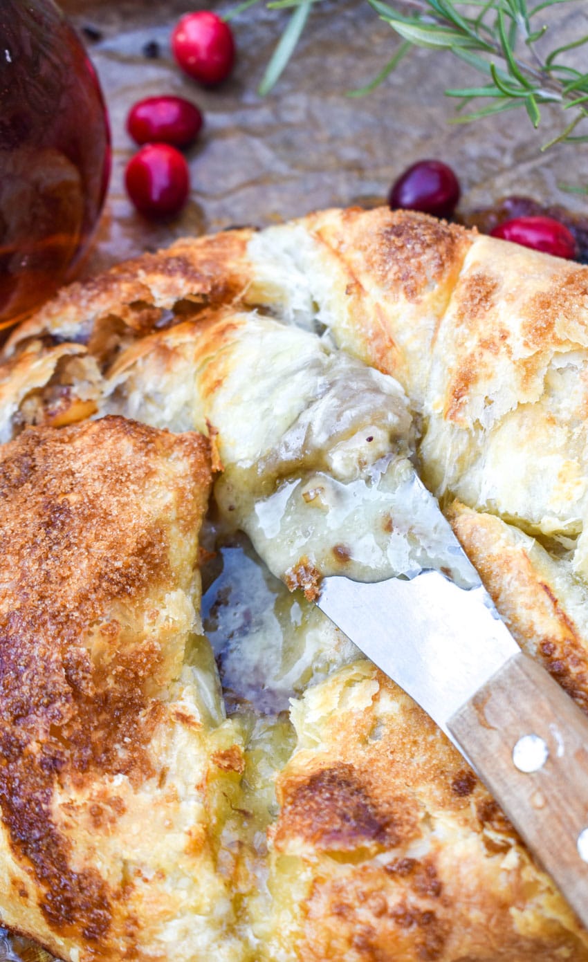 Puff Pastry Wrapped Brie Recipe on a brown parchment paper lined baking sheet with fresh cranberries on the side