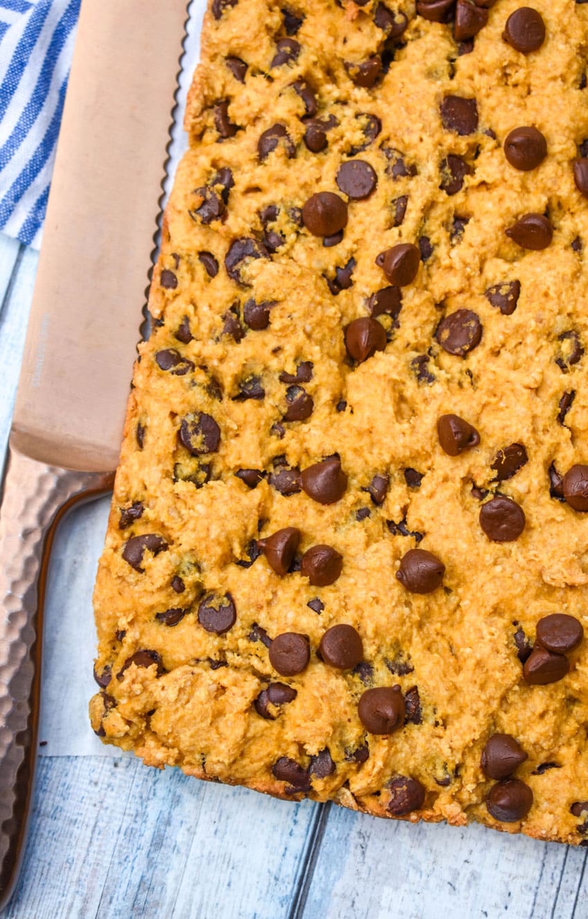 baked pumpkin chocolate chip cookie bar resting on a wooden table with a bronze knife on the side