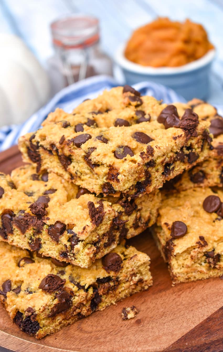 a stack of pumpkin chocolate chip cookie bar squares on a wooden cake stand