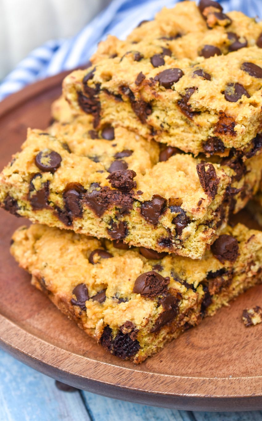 a stack of pumpkin chocolate chip cookie bar squares on a wooden cake stand