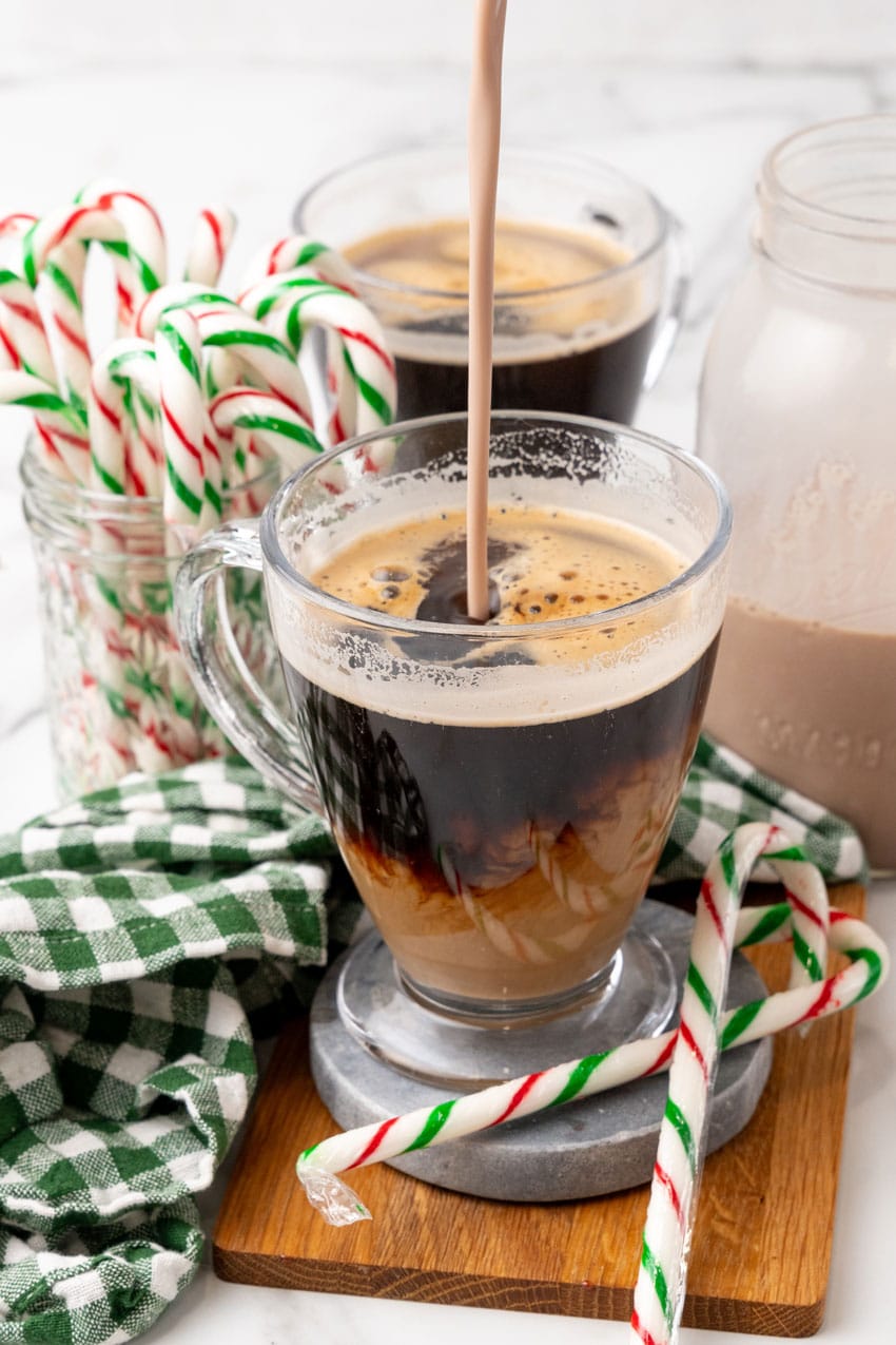 homemade peppermint bark coffee creamer being poured into a glass mug filled with black coffee